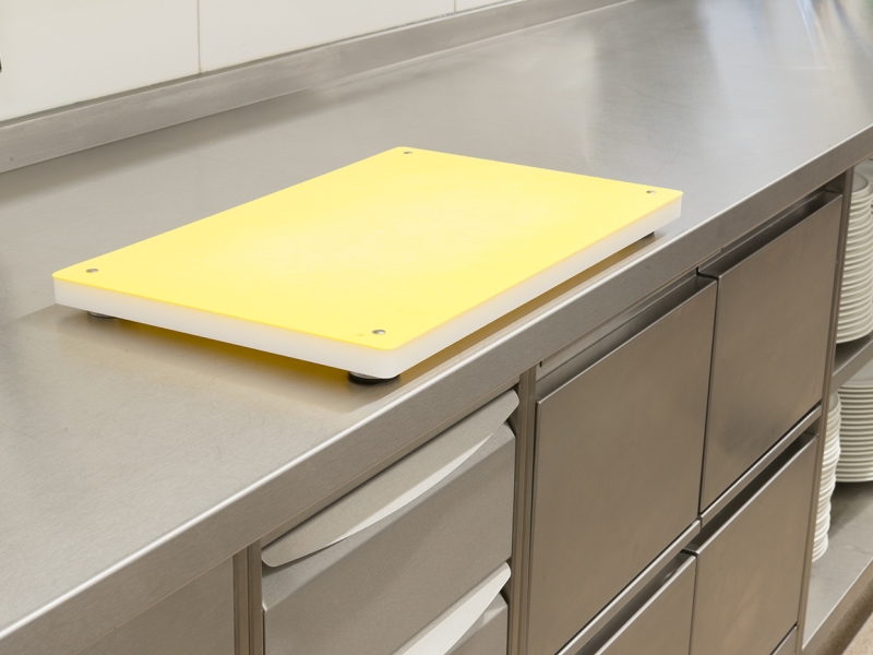 Gelbes Schneidbrett auf Edelstahl-Arbeitsfläche, Unterbau = Arbeitsschränke mit Laden (inkl. Integration bestehender Altmöbel für nachhaltige Weiterverwendung)