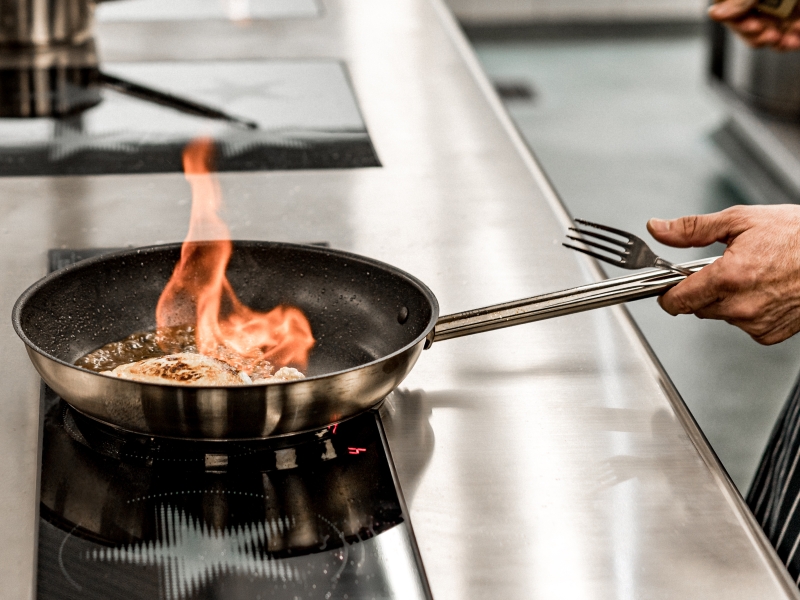 Scharfes Anbraten mit Flamme in der Bratpfanne am Induktionskochfeld (Edelstahl-Kochblock)