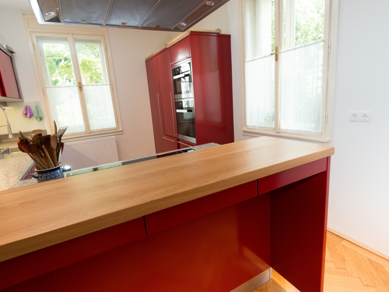 Gesamt-Aufnahme von Küche inklusive Wandhängeschrank und Hochschrankverbau mit integriertem Backrohr und Dampfbackofen und erhöhter Ess-Bar