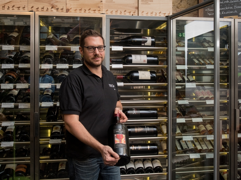 Mitarbeiter der Selektion Vinothek Burgenland präsentiert eine Flasche Wein aus der raumlangen Weinvitrine